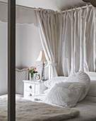 White cushions and fur blanket on four postered bed with cut roses and lamp at bedside