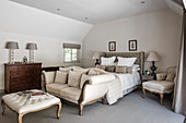 Cremefarbenes Zwei-Sitzer-Sofa am Fußende des Doppelbetts, Holzkommode mit zwei Lampen