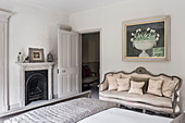 Viktorianischer Kamin mit neu gepolstertem antiken Sofa unter Kunstwerken im Schlafzimmer