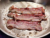 Bacon being fried in a pan