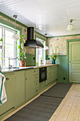Green base units and nostalgic wallpaper in the kitchen