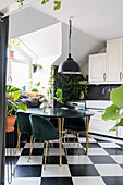 Table with black top and upholstered chairs in kitchen with chequered floor