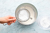 Icing sugar being sifted into a bowl