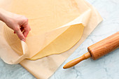 Pastry being rolled out between two layers of baking paper