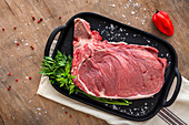 Fresh raw T-bone beef steak with red pepper, tomato, pink pepper and parsley ready to cook