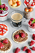 Glass cup of coffee with chia pudding garnished with raspberries and white cherries with wheat crispbreads with nut spread and jam with almond pieces
