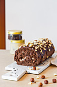 Homemade roll cake with chocolate glaze and hazelnut placed on chopping board in modern kitchen