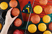 Crop anonymous female putting freshly baked colorful cupcakes from baking pan on metal grid while preparing pastry for christmas party