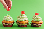 Cupcakes mit grün gefärbter Schlagsahne und Cocktailkirschen zu Weihnachten