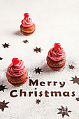 Sweet cupcakes with pink frosting arranged on table sprinkled with sugar powder and decorated with stars and merry christmas text