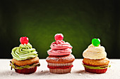 Yummy festive Christmas cupcakes decorated with colorful frosting and cherry berries placed on table sprinkled with white sugar powder against green background