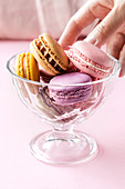 Crop female taking colorful tasty macarons from glass bowl placed on table in kitchen