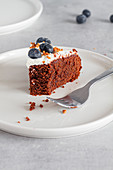 Slice of homemade chocolate sponge cake topped with fresh whipped cream and whole blueberries