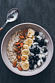 Bowl of porridge with raw almonds, sliced banana, blueberries and grated coconut
