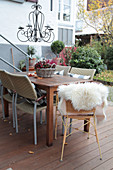 Terrace table decorated for autumn with chandelier, flowers in a basket planter, and sheepskin