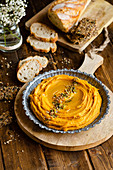 Appetizing hummus with sweet potato arranged on wooden table with bread in kitchen for lunch