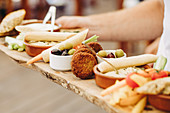 Crop anonymous person holding rustic wooden tray with various types of appetizers during party