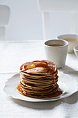 Stack of pancakes drizzled with maple syrup on a small white cake stand