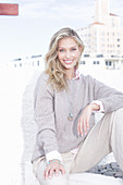 Junge blonde Frau in hellem Pullover und Hose am Strand