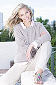 A young blonde woman on the beach wearing a light jumper and trousers