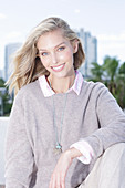 A young blonde woman on the beach wearing a light jumper and trousers