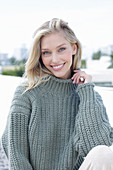 A young blonde woman on the beach wearing a grey knitted jumper