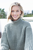 A young blonde woman on the beach wearing a grey knitted jumper