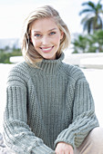 A young blonde woman on the beach wearing a grey knitted jumper
