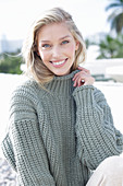 A young blonde woman on the beach wearing a grey knitted jumper