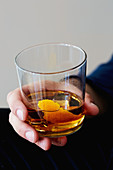 Mann hält Glas mit Whisky und Orangenschale