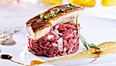 Juicy steak tartare with white onion served with glazed piece of foie gras on white plate with sauces