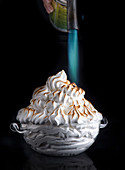 Process of browning fresh meringue pile over baked vanilla souffle in crystal bowl