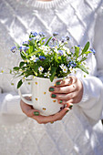 Frau hält Tasse mit Frühlingsstrauß aus Sternmiere und Vergißmeinnicht