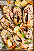 Roasted salmon steaks with aromatic herbs and spices garnished with lemon slices on metal baking tray