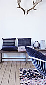 Wooden bench with cushions below antlers on white wall