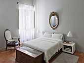 Goldrahmenspiegel über Doppelbett und Truhe im Schlafzimmer mit hellgrauen Wänden
