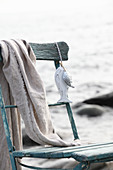 Verwitterter Holzstuhl mit Fischanhänger und Tuch am Strand