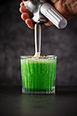 Bartender adding foam to green lime cocktail
