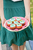 Frau hält Teller mit bunten Muffins mit Regenbogen-Deko