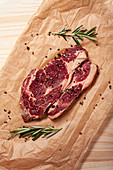 Raw rib eye beef steak with fresh rosemary and pepper