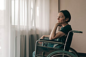 Depressed woman in wheelchair looking out the window