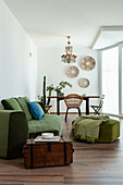 Old wooden chest used as side table and green upholstered furniture in open-plan living room