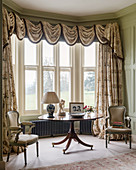 Table and Baroque chairs in bay window with opulent curtains