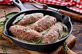Ground beef rolls with sauce and herbs in pan