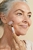 A grey-haired woman using a face roller