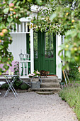 Cat on terrace outside green exterior door leading into summery garden