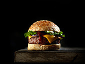 Burger mit Käse und Salat vor schwarzem Hintergrund