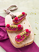 raspberry eclairs with pistachio nuts on a wooden board