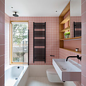 Bathtub below window in bathroom with pink wall tiles
