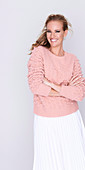 A young woman with long, brunette hair wearing a pink jumper and a pleated skirt